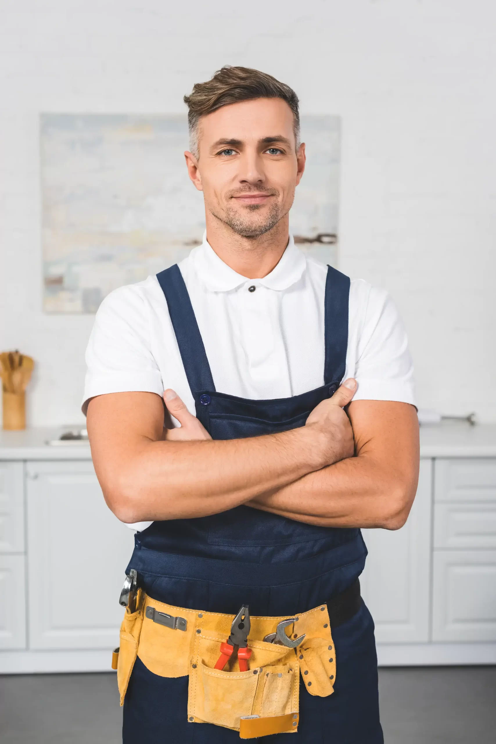 A repairman in tool belt standing with crossed arms smiling.