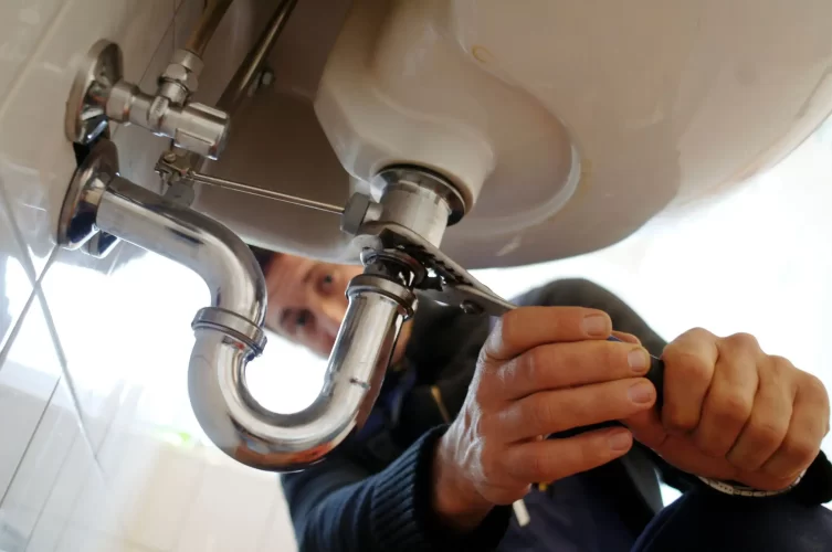 A close up image of a plumber fixing the sink with work tool.