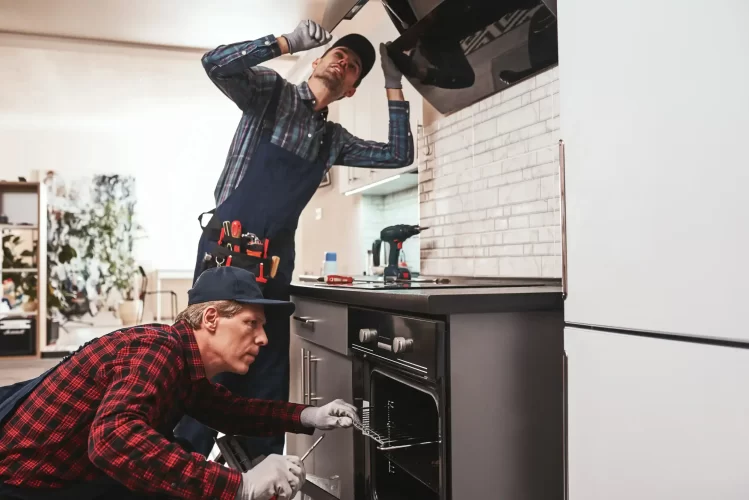 Two workers repairing the stove and oven malfunctions.
