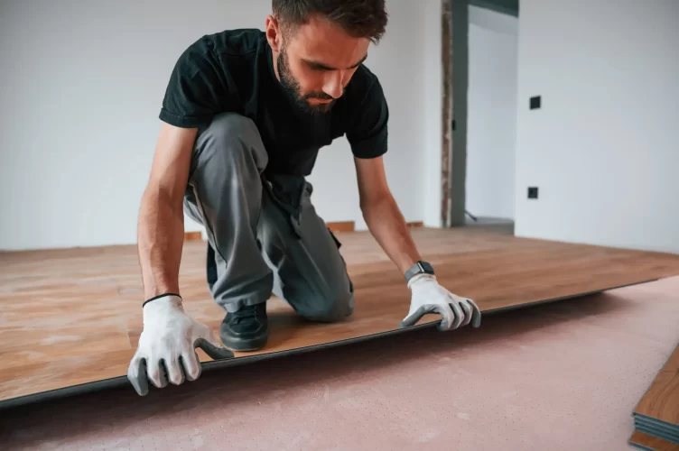 A man installing a wood tile base on the floor of the client's house.