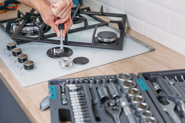A workers hand repairs a hotplate of a gas panel.