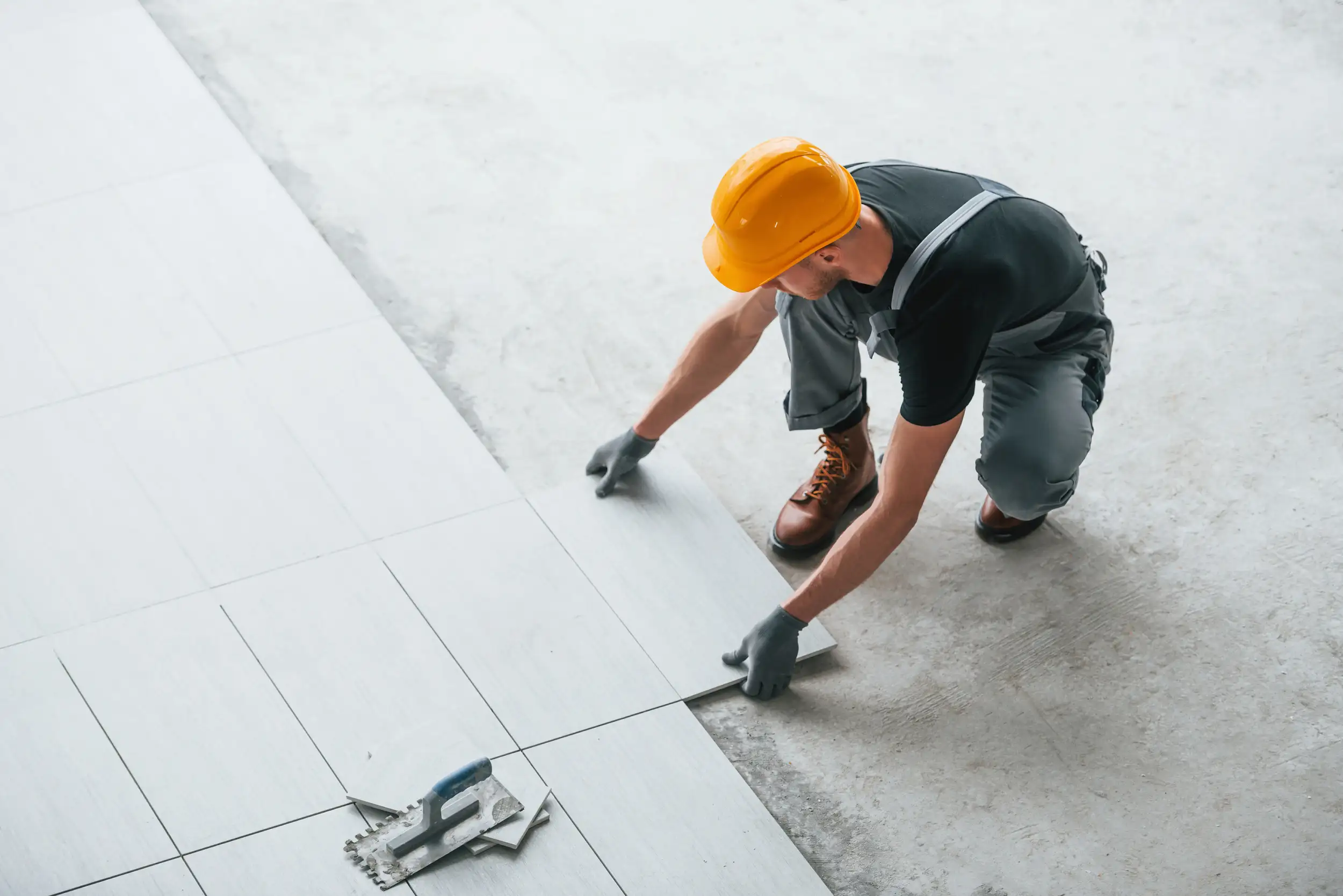 A top view of a construction worker placing a tile on the floor of project building.